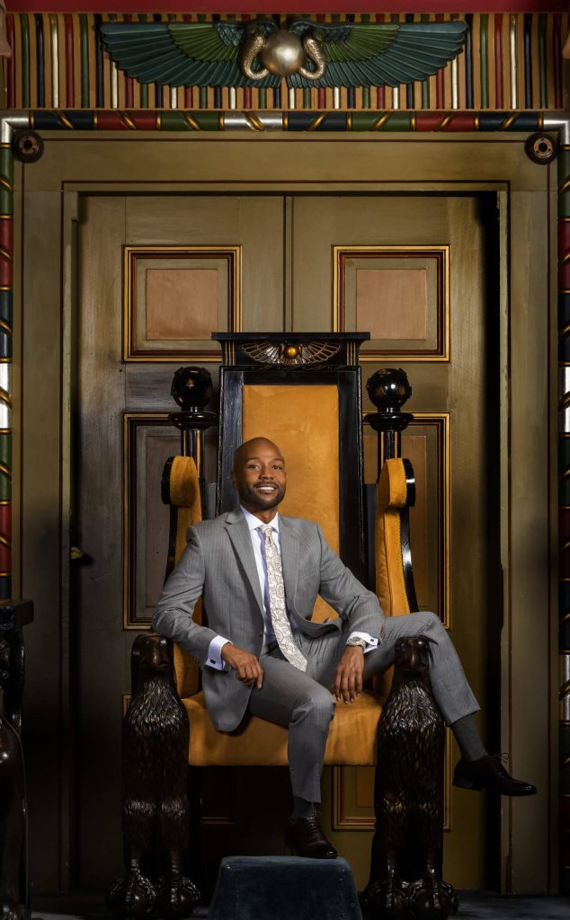 Personal branding photographer taking a photo of a black man in a suit sitting in a chair in front of large doors