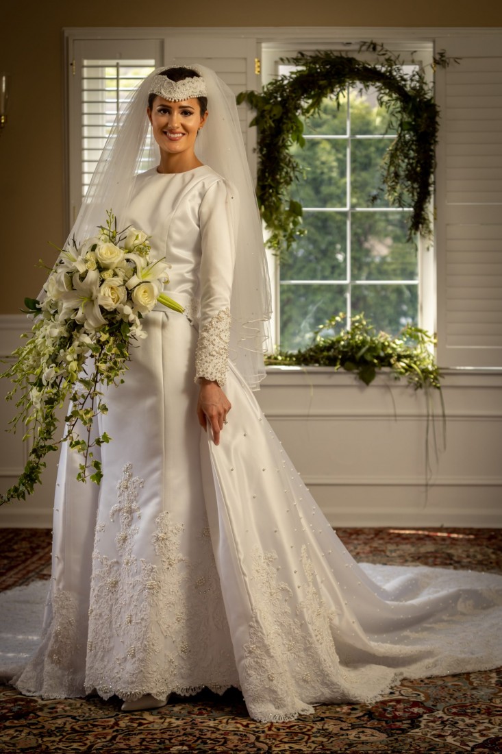 The bridal dress is a custom design from James May in Philadelphia. It features intricate floral patterns, small pearls, and traditional white lace along the edge.  This elegant wedding dress is fitting for the Spring, and the white flower bouquet compliments the delicate designs. The handsewn flowers at the bottom of the skirt make the design appropriate for a Spring wedding.  Getting ready photos of the bride show her anticipation on the big day. These portraits capture the beginning of the story.