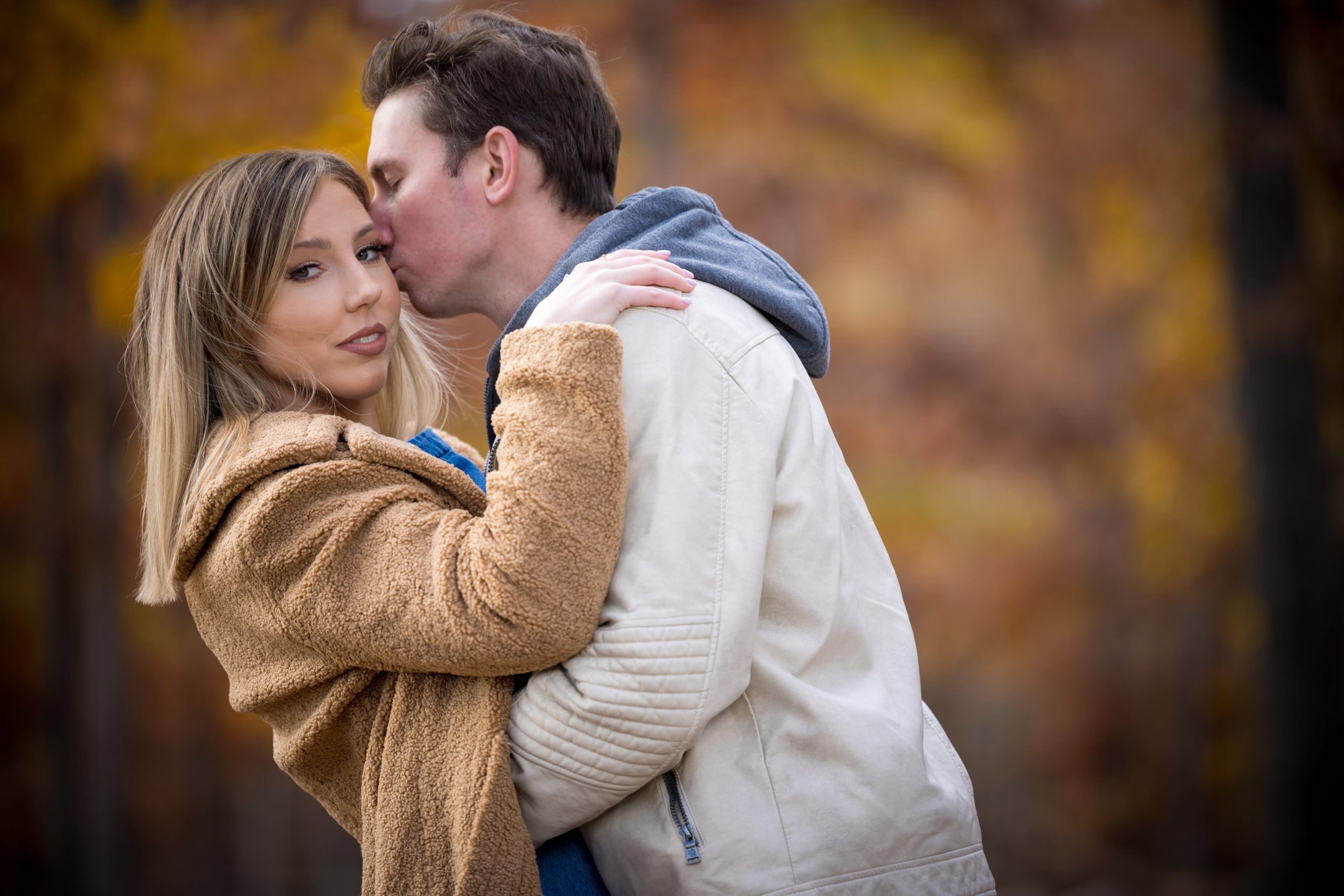 man in white leather jacket kissing a woman in brown fur jacket on the cheek