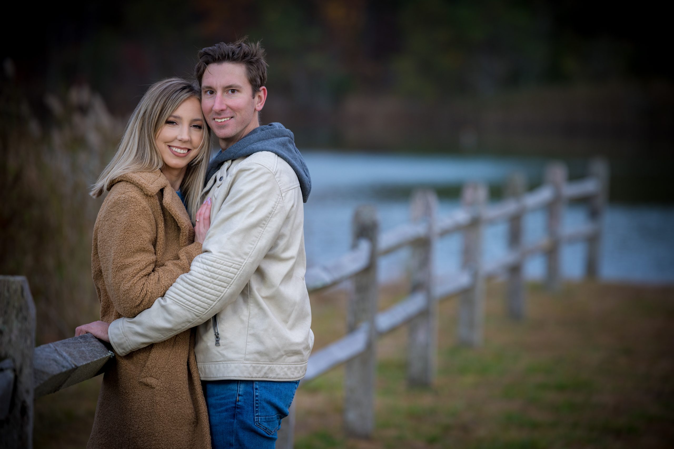 man and woman posing by a wooden fence and a lake at autumn lake winery in nj