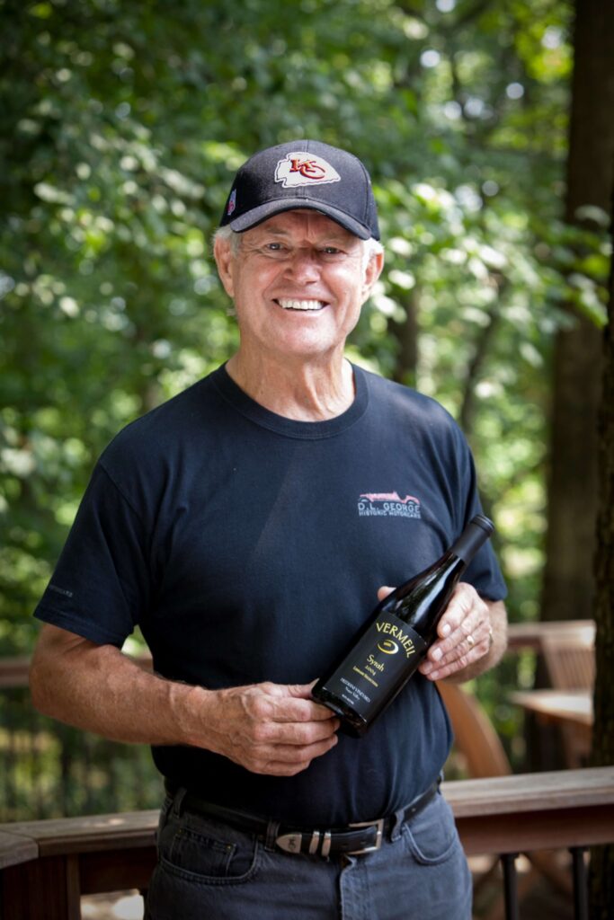 dick vermeil posing with wine bottle and wearing a black kansas city chiefs hat
