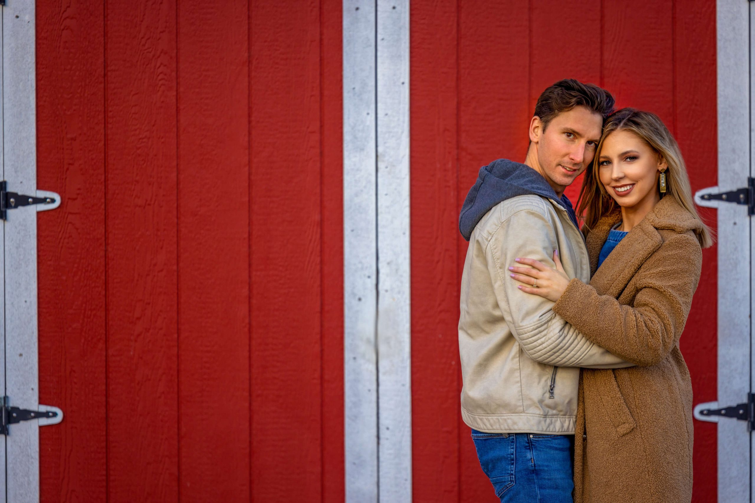 man and woman hugging each other against a red shed