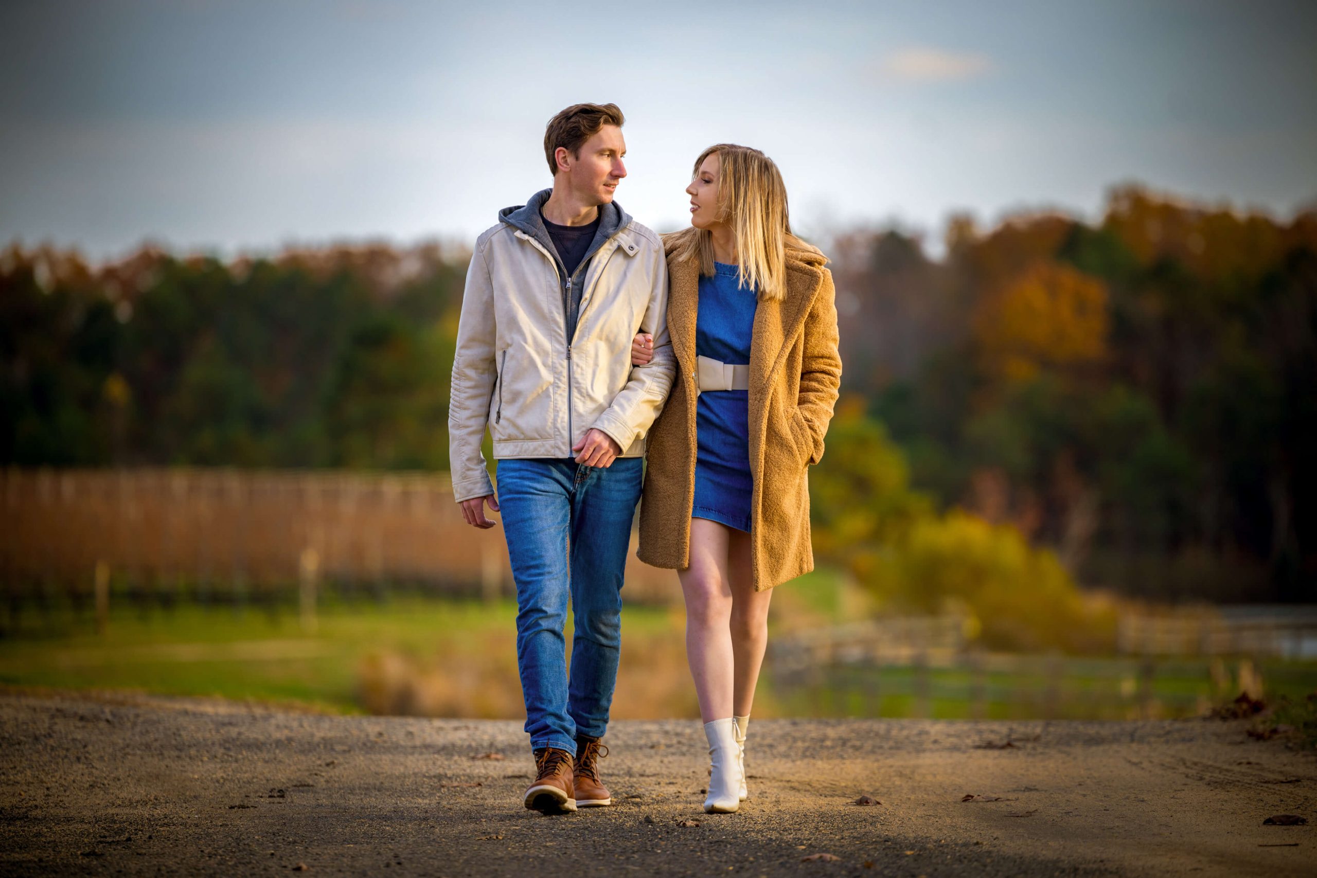 engaged couple walking on dirt road together during golden hour sunset