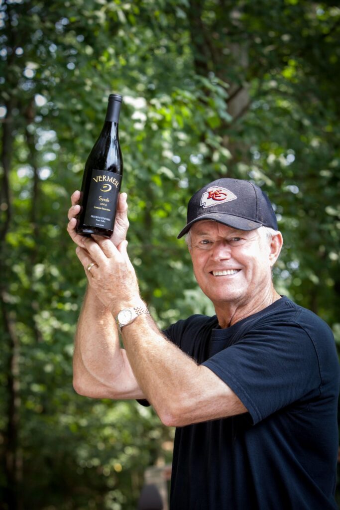 dick vermeil holding a syrah wine bottle