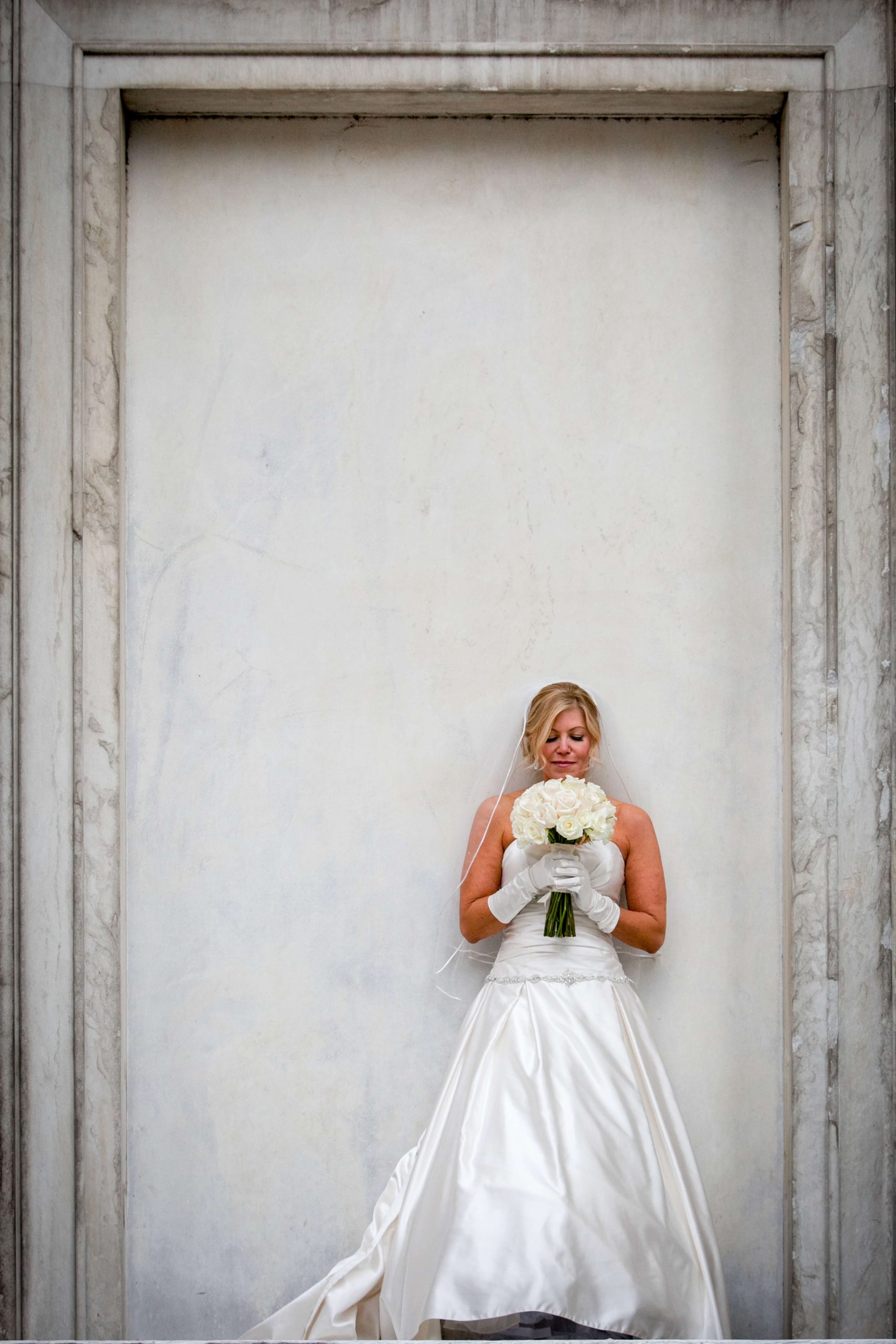 bride holding flower bouquet against white wall