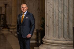 man in suit with orange tie by white roman column