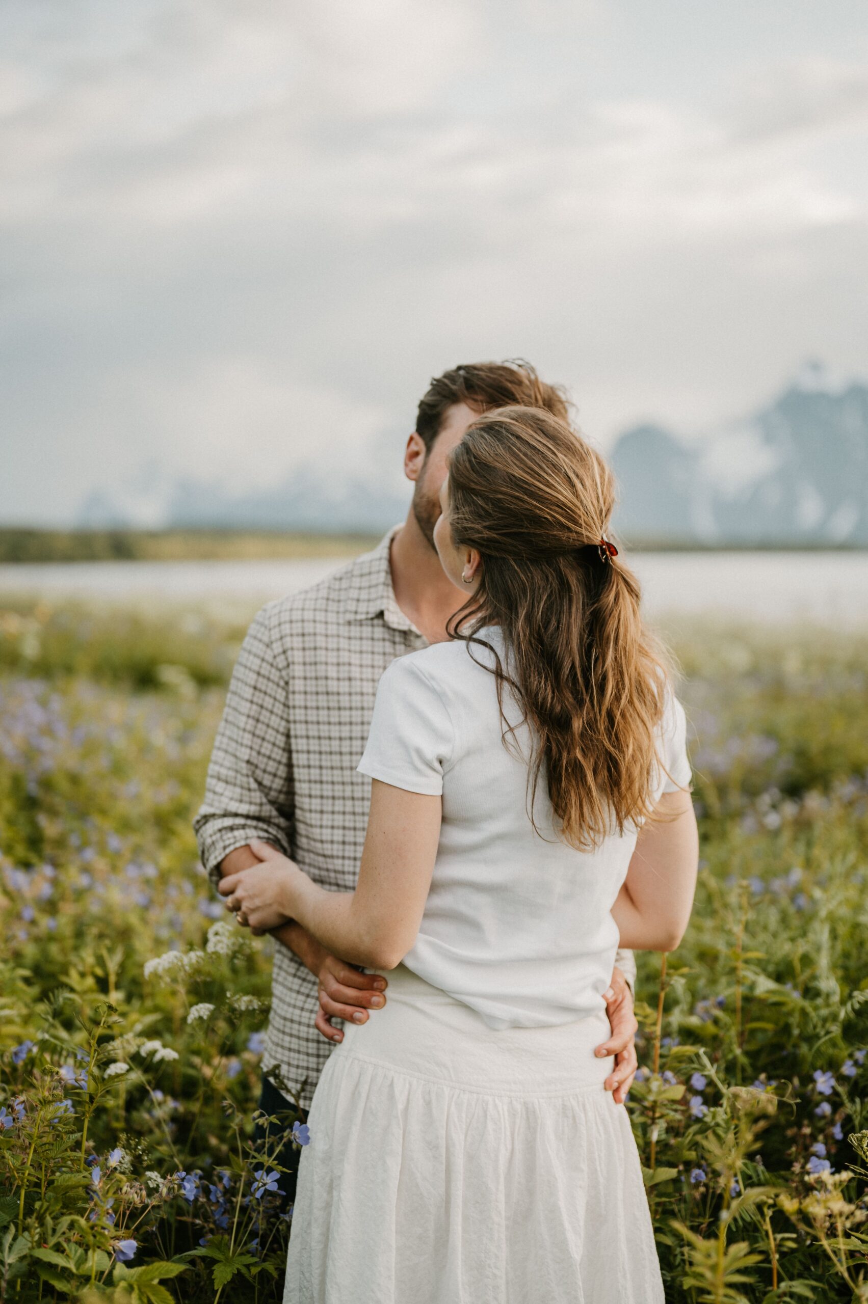 man and woman embrace by creek with reflection in water