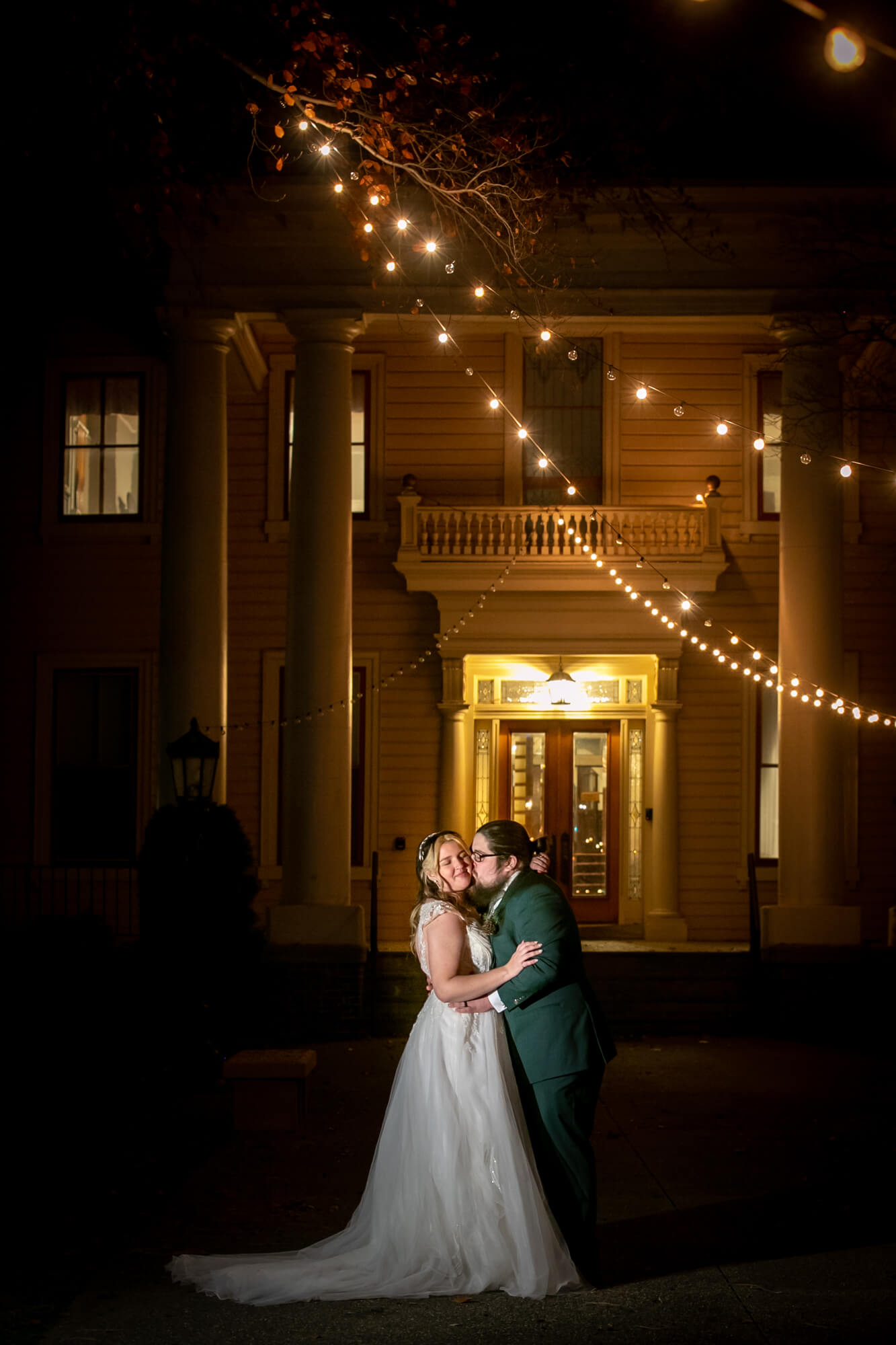 bride and groom at mansion under string lights