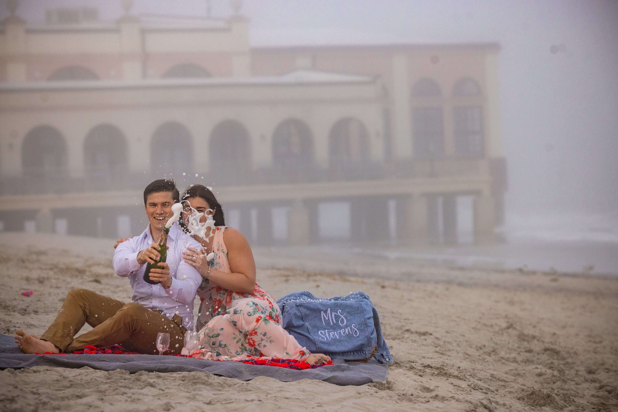 couple pops champagne during picnic on the beach