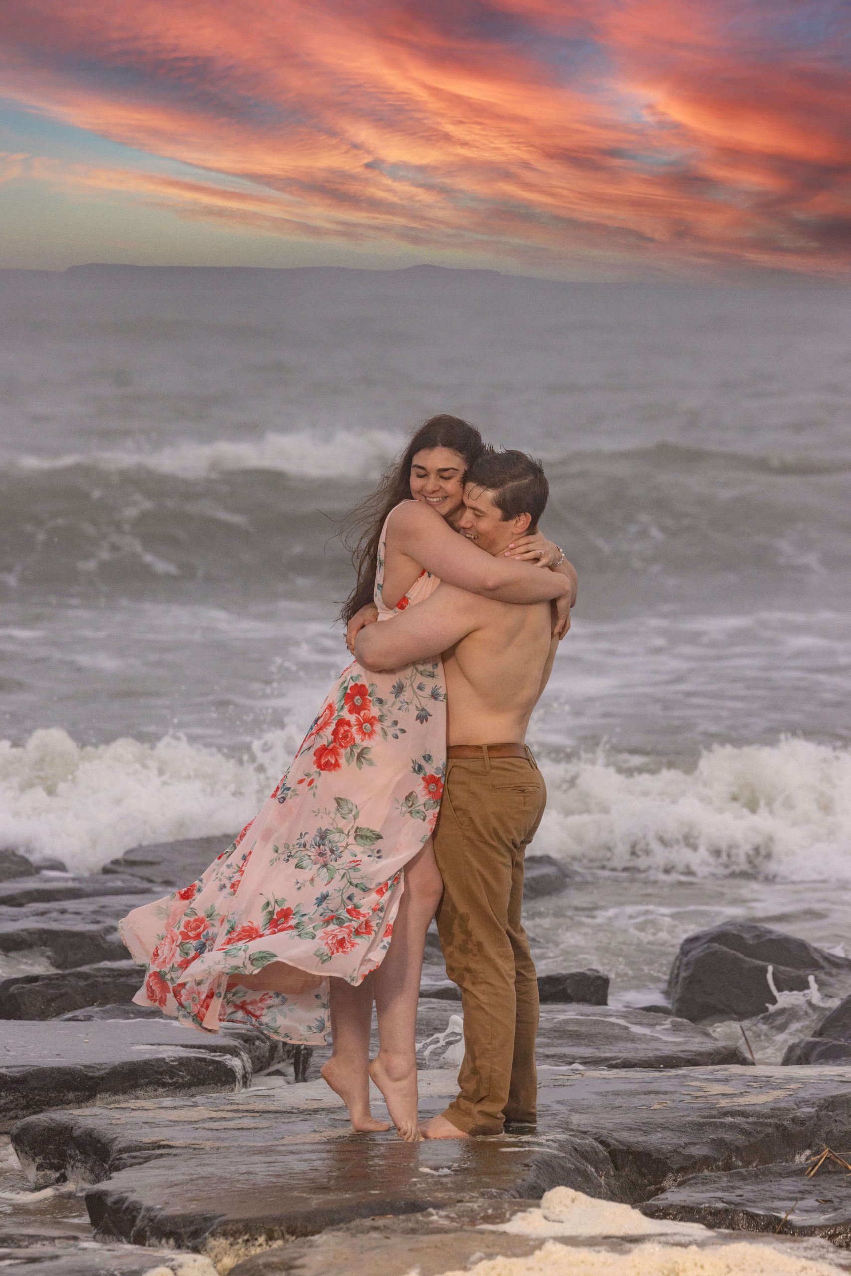 man and woman embrace by crashing waves at beach