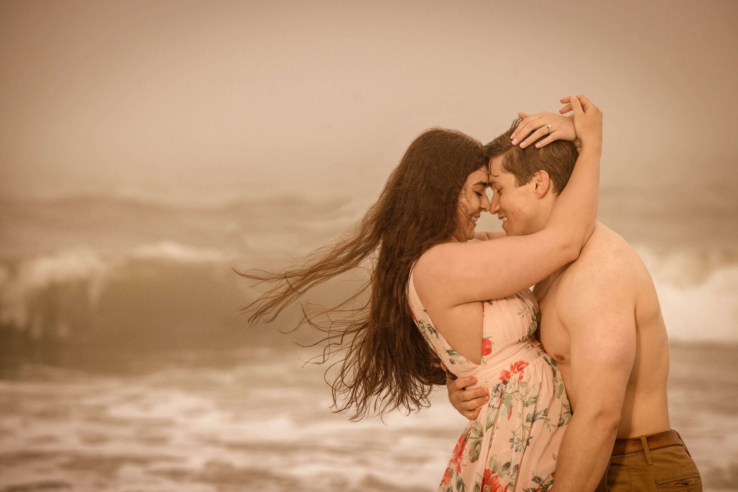 man and woman embrace by crashing waves at beach