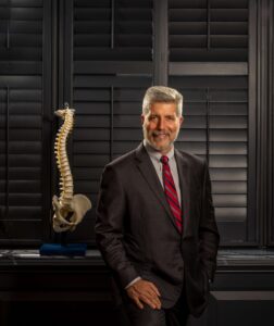 man in suit poses next to spine skeleton replica
