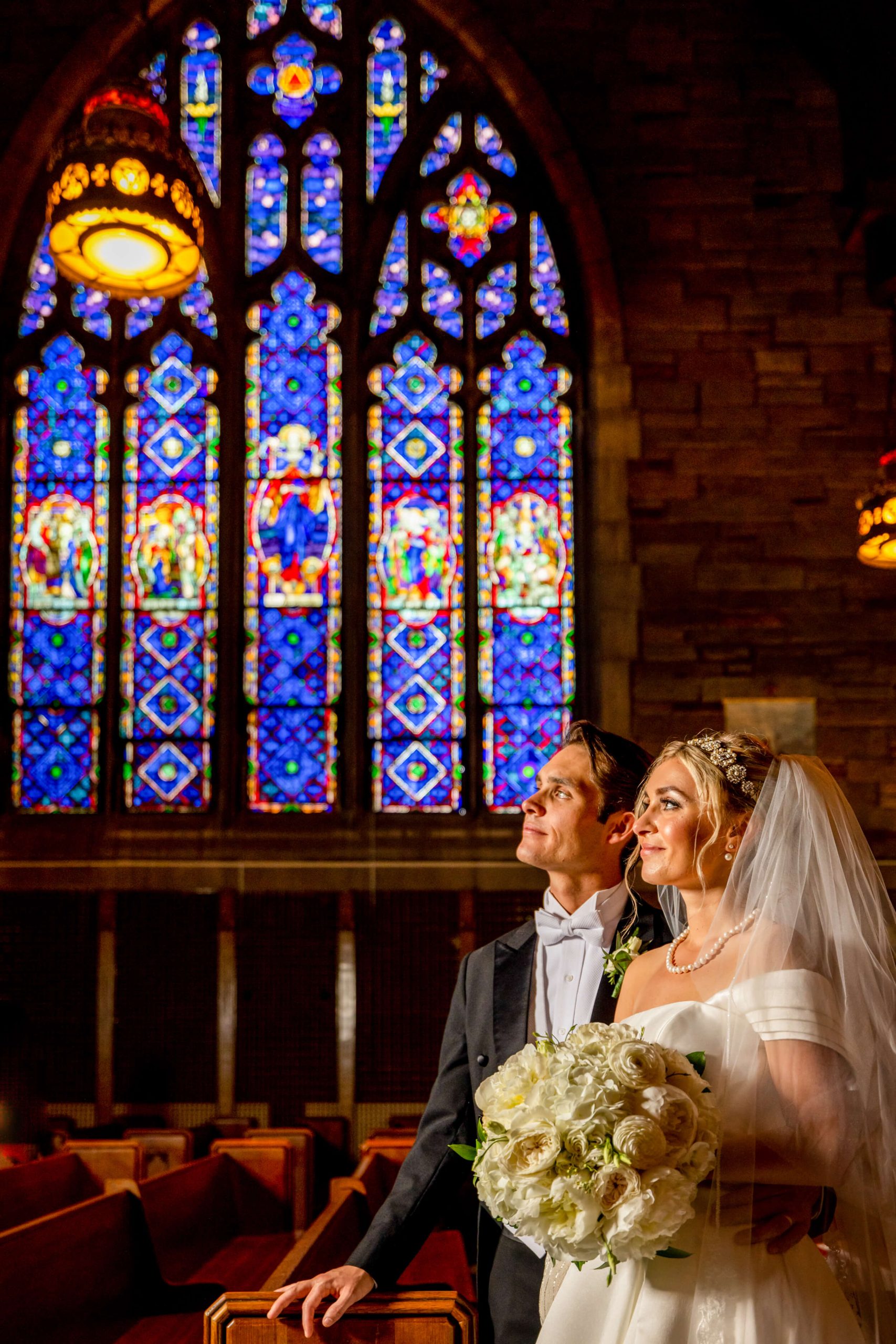 bride and groom pose against stained glass window