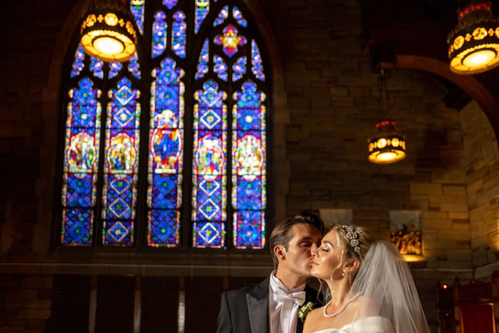 bride and groom kissing against stained glass window in church