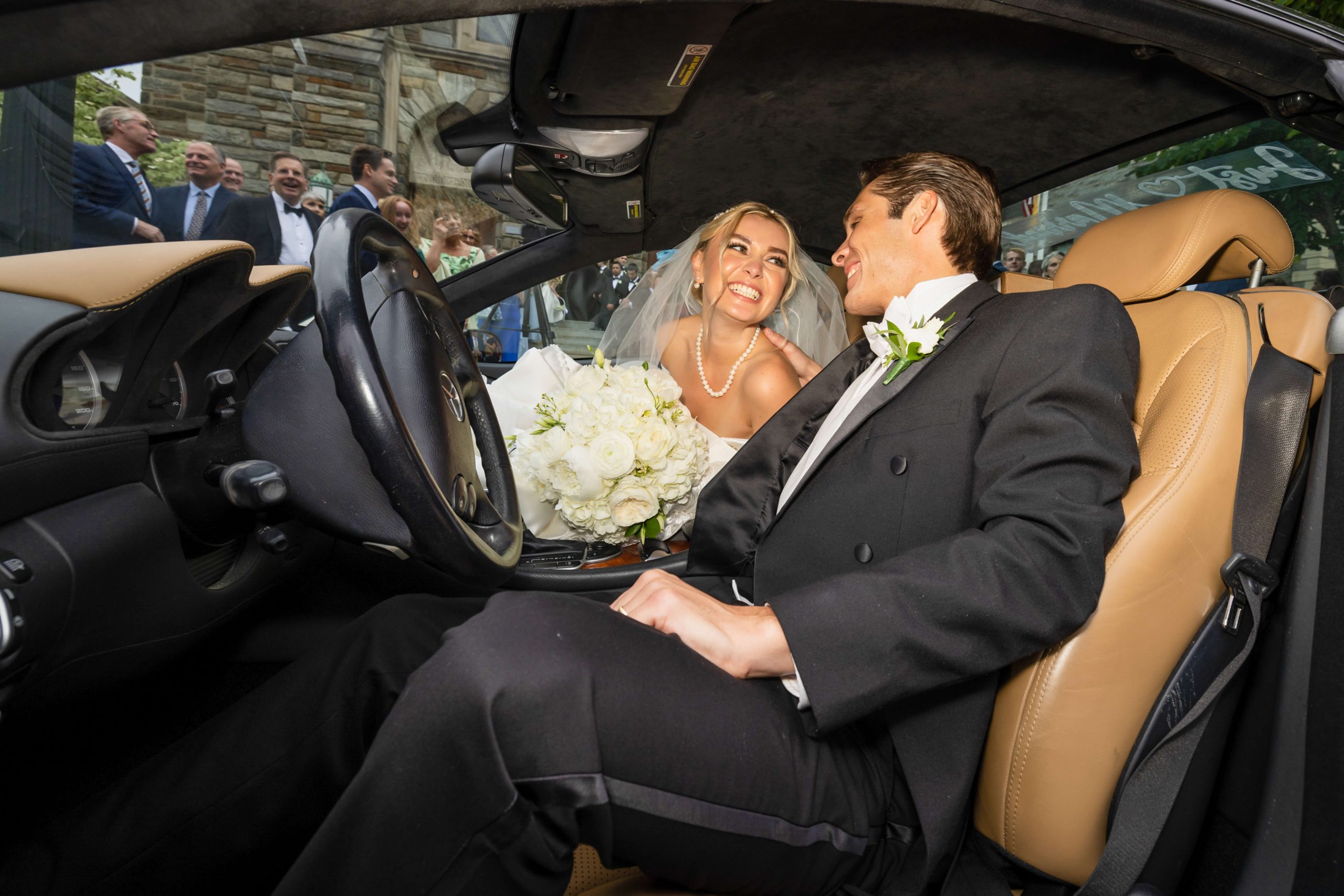 bride and groom smile in mercedes car after wedding