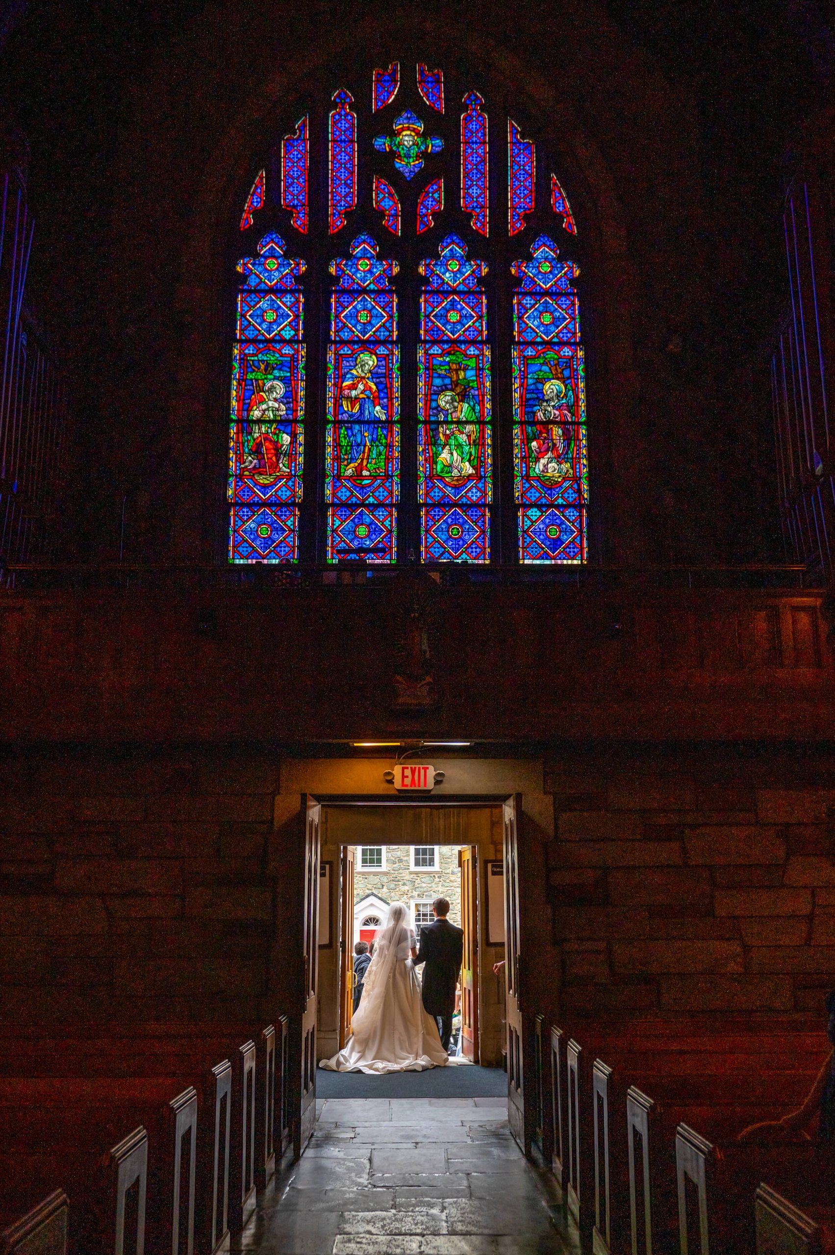 bride and groom exit church with stained glass window