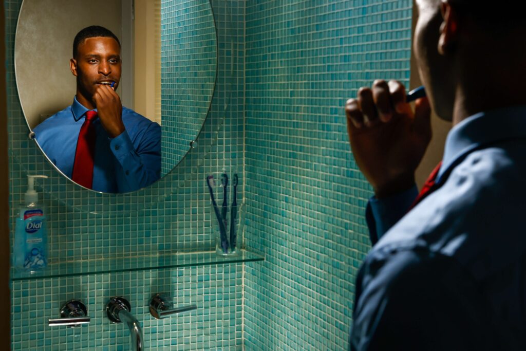 man wearing a red tie and brushing his teeth in the mirror