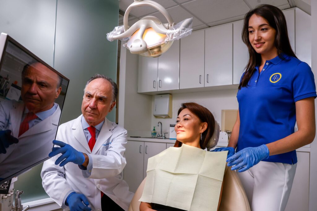 dentist and assistant looking at a computer screen with a patient as the patient sits in an operating chair