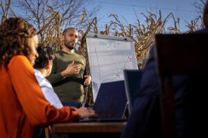 man showing statistics on a white board at business meeting in cornfield