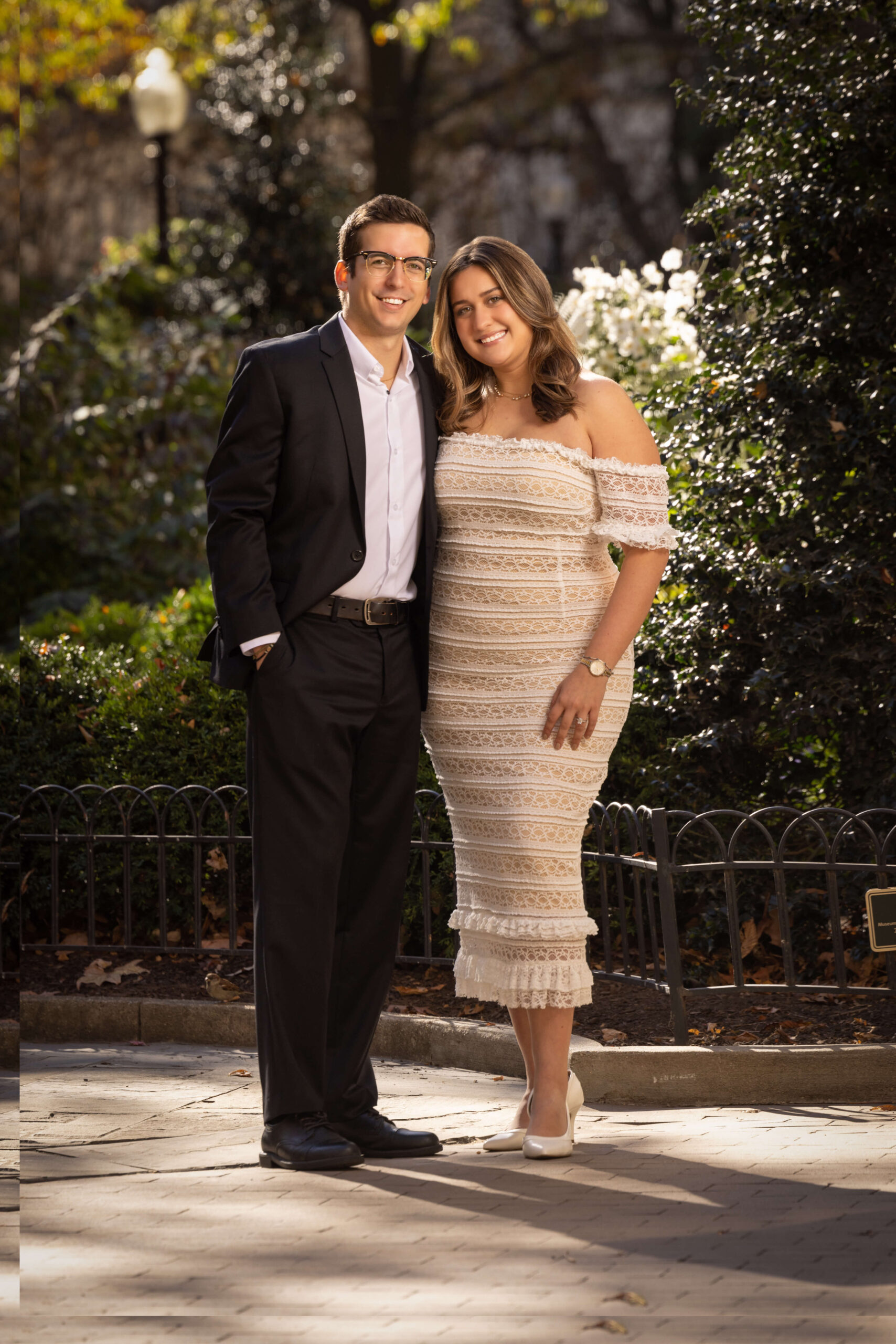 man in suit and woman in dress smiling in park