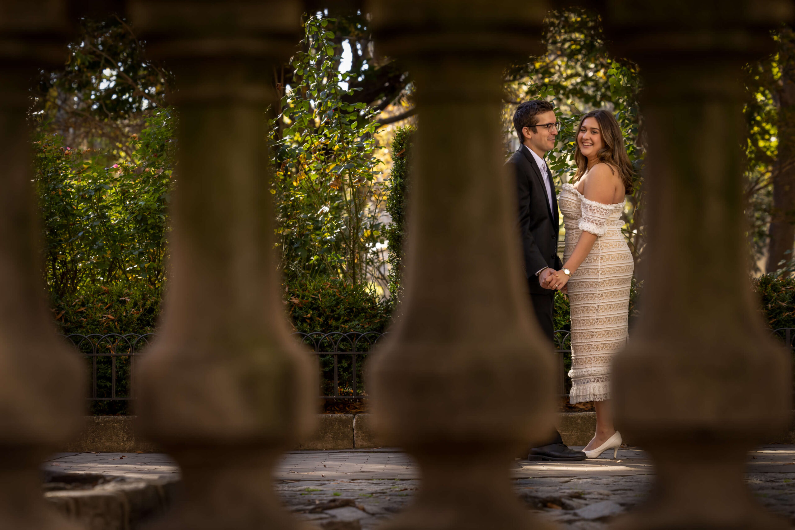 couple holding hands through grey railings in park