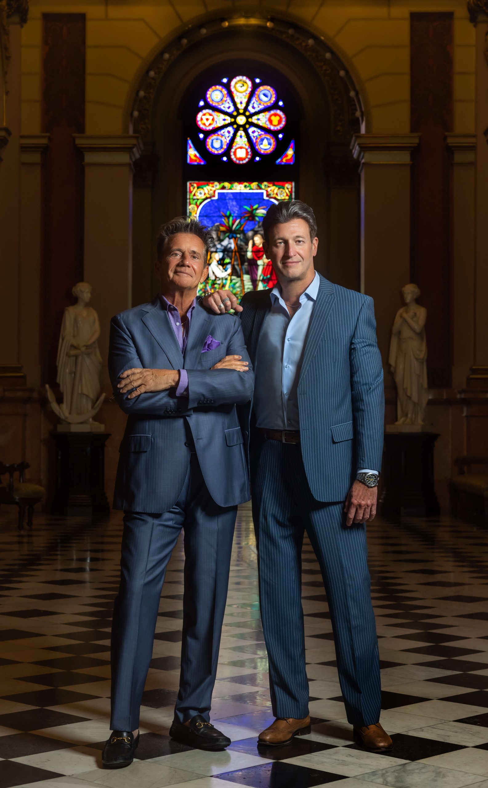 two men in suits standing in masonic temple with stained glass window