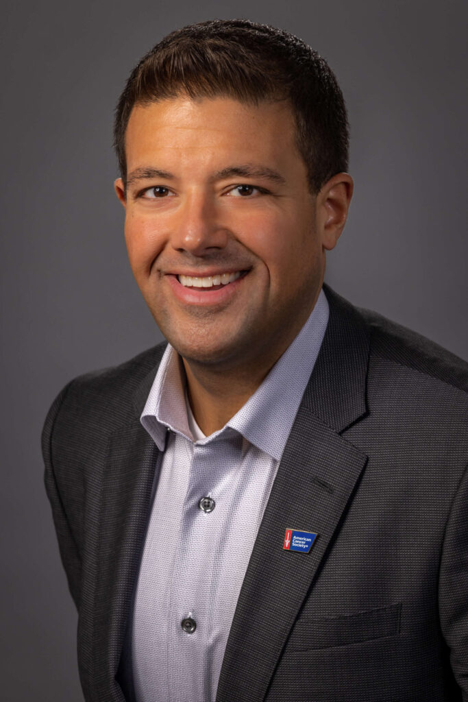 man smiling in black suit with purple button down