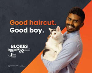 man in blue shirt smiling while holding a black and white cat