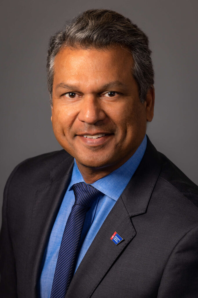 man smiling in black suit with blue tie