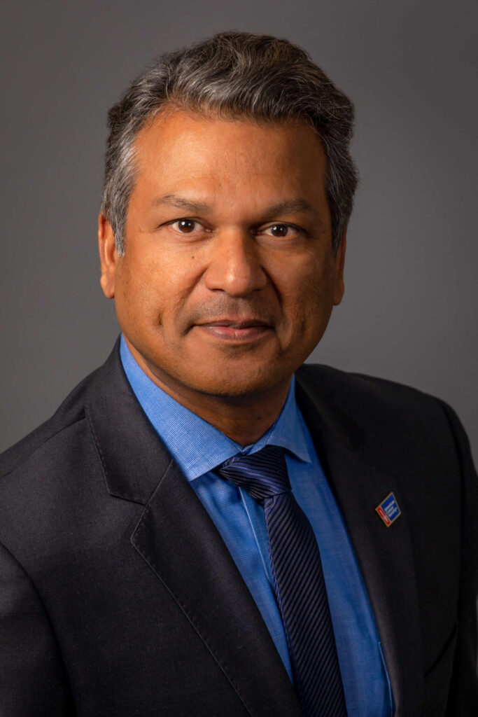 man with serious expression in a black suit with blue tie