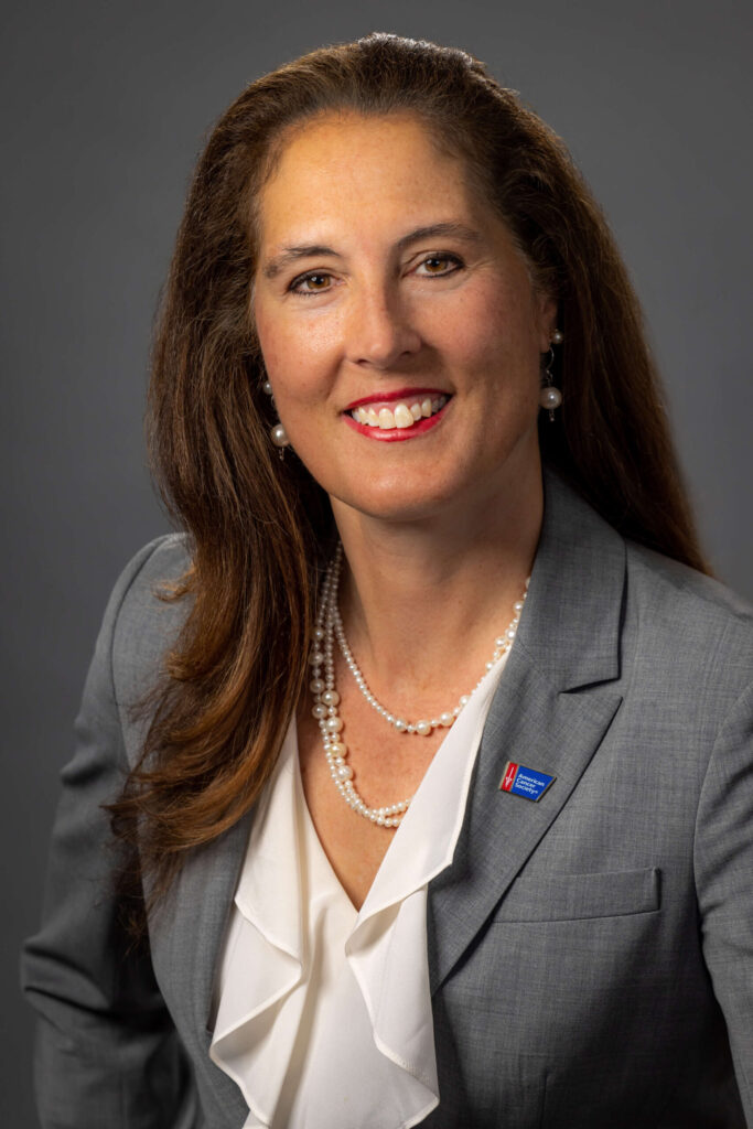 woman smiling in gray suit with pearl necklaces and earrings