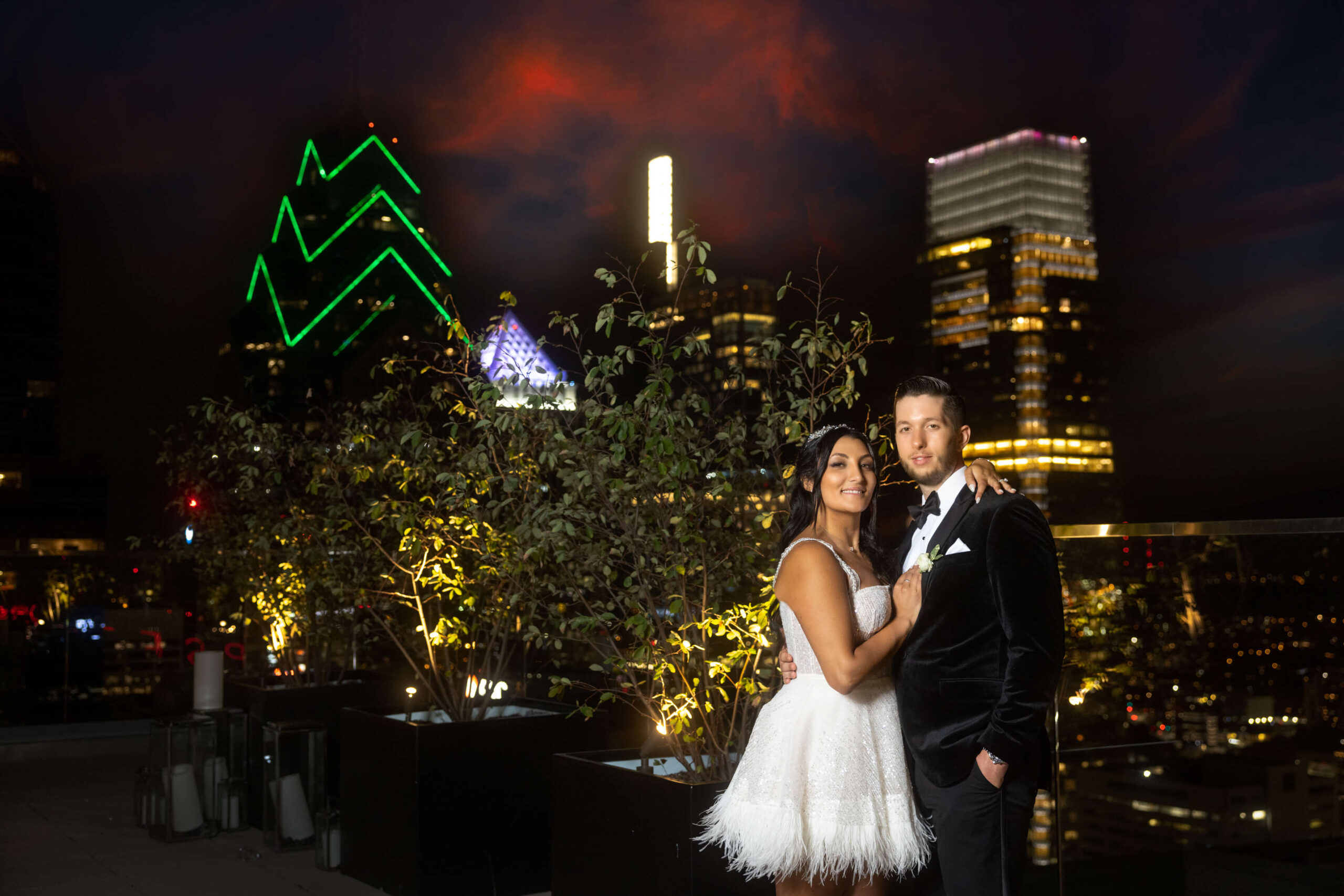 bride and groom posing with philadelphia skyline at night on wedding day