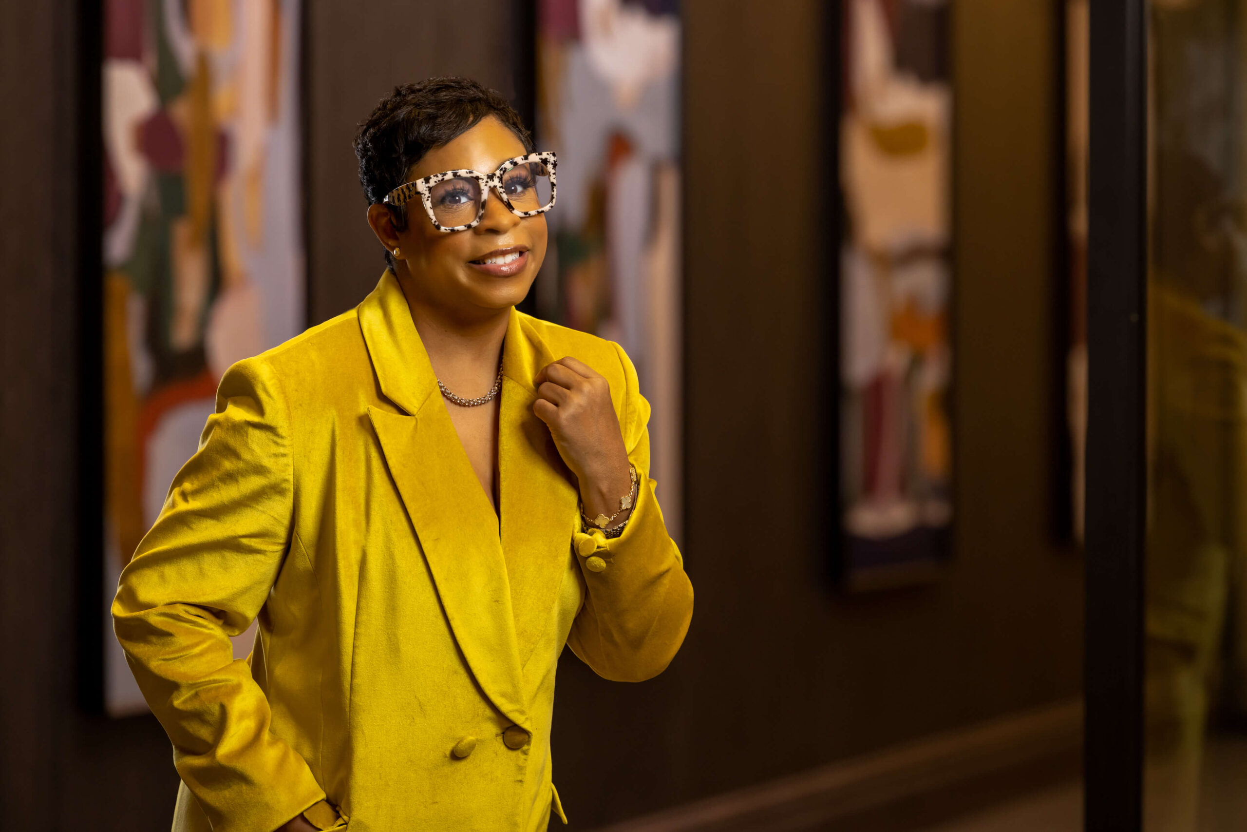 woman with short hair wearing a mustard yellow blazer and tortoise shell glasses