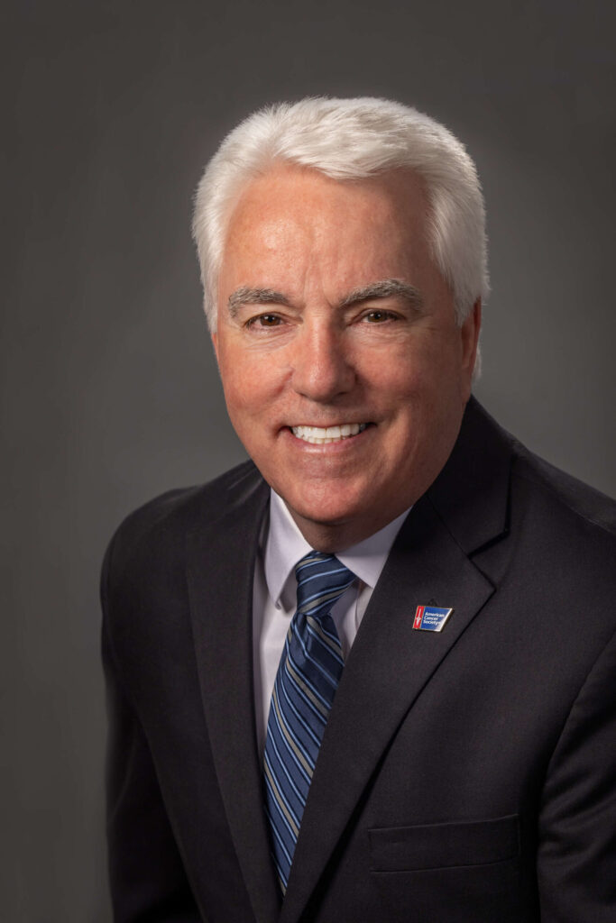 man smiling with white hair in black suit