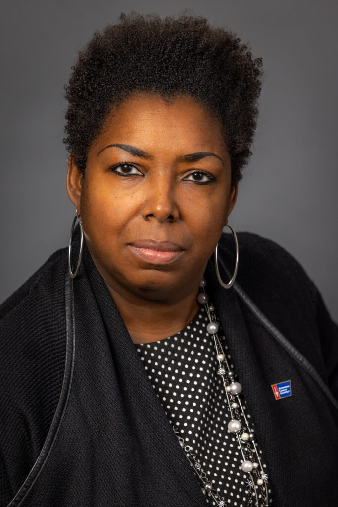 serious woman with red and blue pin against gray background