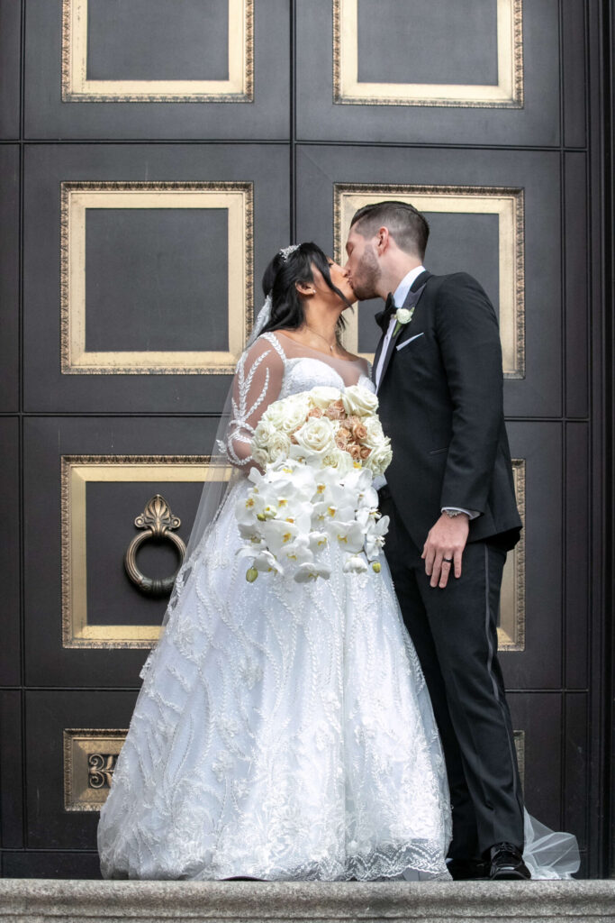 bride and groom kiss in front of dramatic black and gold doors at philly cathedral