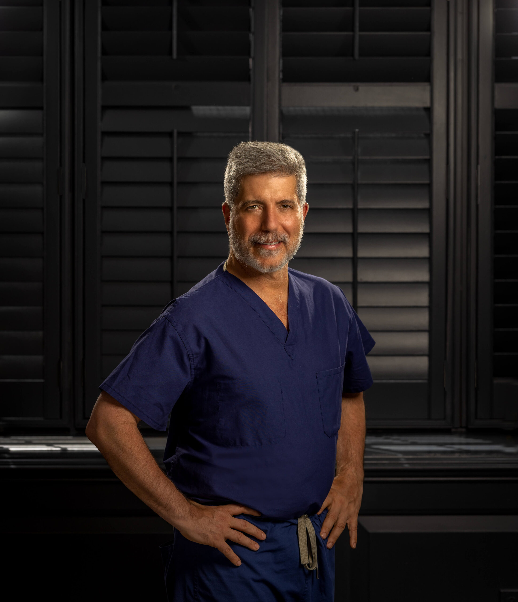 dr. alex vacarro in blue scrubs with hands on hips against black shutters