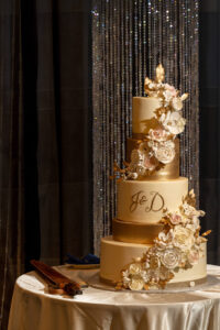 tall, gold and white wedding cake with edible florals. diamonds dazzle in the background and sword lies on table in sheath.