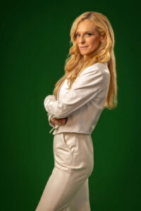 blonde woman with serious expression and folding arms against green background