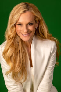 smiling blonde woman in ivory white outfit against green background