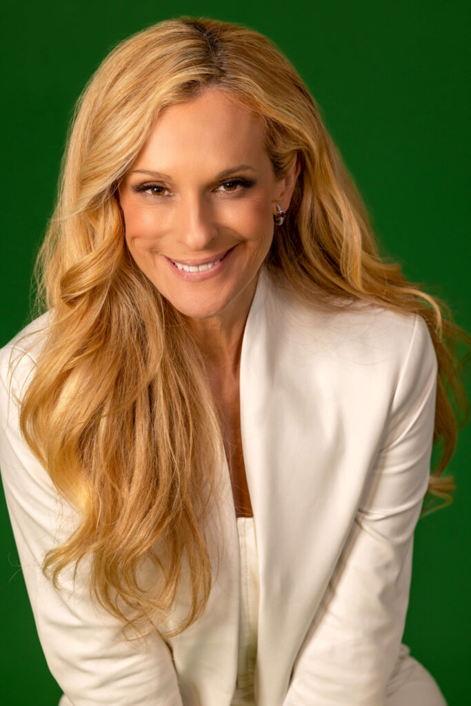 smiling blonde woman in ivory white outfit against green background