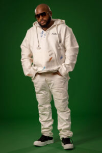 man in white hoodie, ripped jeans with hands in pockets against emerald green background