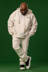 man in white outfit with black sneaker and sunglasses looking at floor with hands in pockets