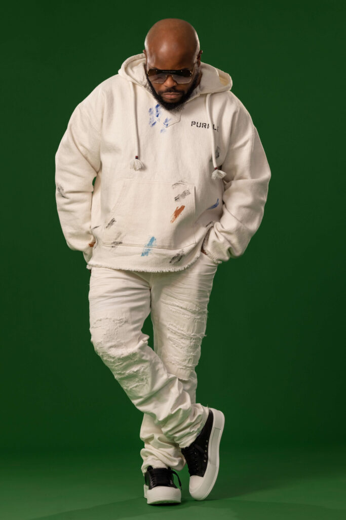 man in white outfit with black sneaker and sunglasses looking at floor with hands in pockets