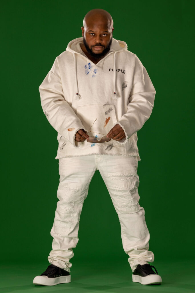 man with serious expression in white hoodie removing sunglasses