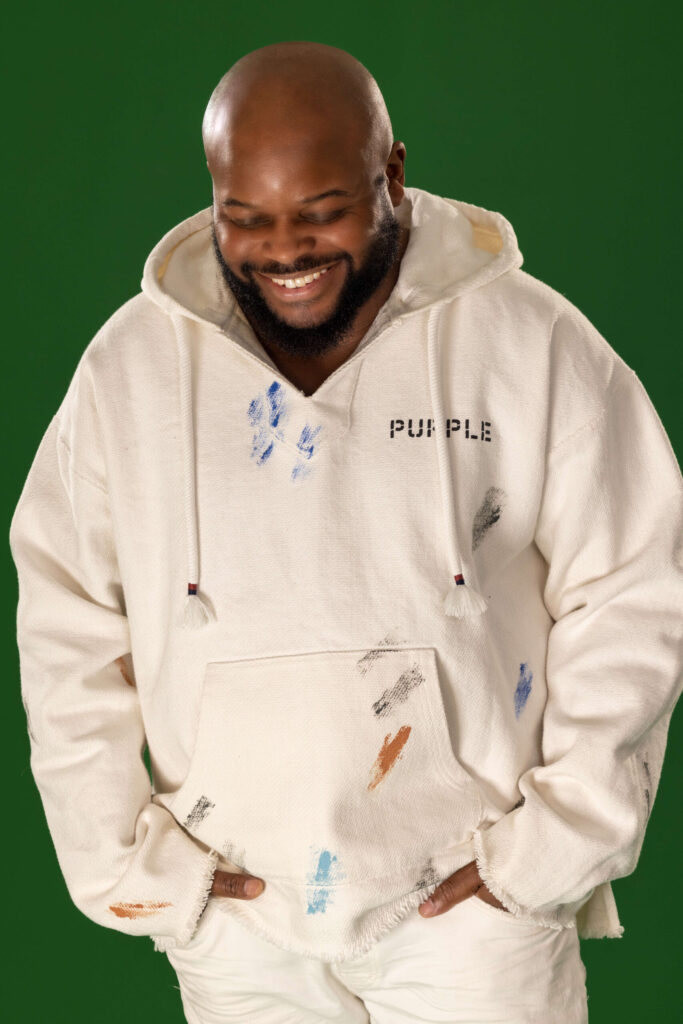 man with hands in pockets in a white hoodie laughing and smiling