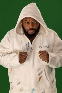 man pulling strings of a white street hoodie against a green background