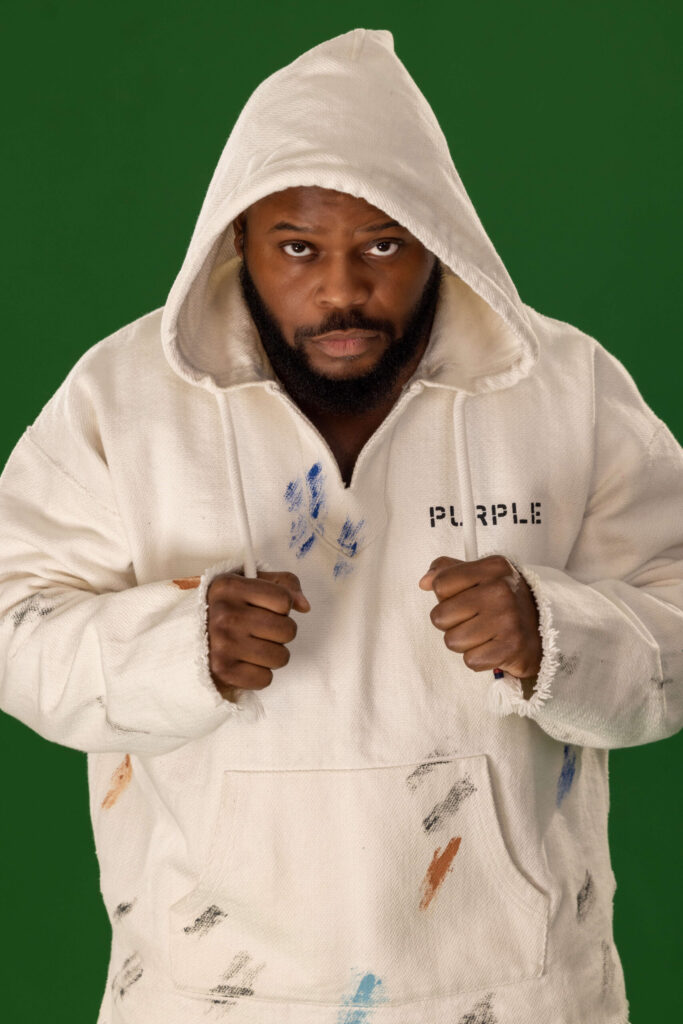 man pulling strings of a white street hoodie against a green background