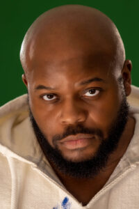 man with beard in white hoodie with serious expression against a green background