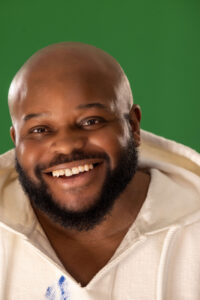man with beard in white hoodie smiling against a green background